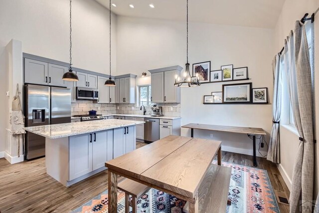 kitchen with light stone counters, gray cabinetry, stainless steel appliances, a kitchen island, and decorative light fixtures