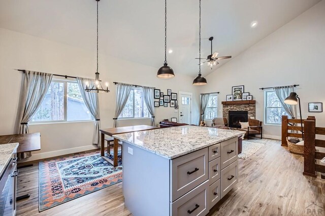 kitchen with high vaulted ceiling, a stone fireplace, a kitchen island, light wood-style floors, and decorative light fixtures