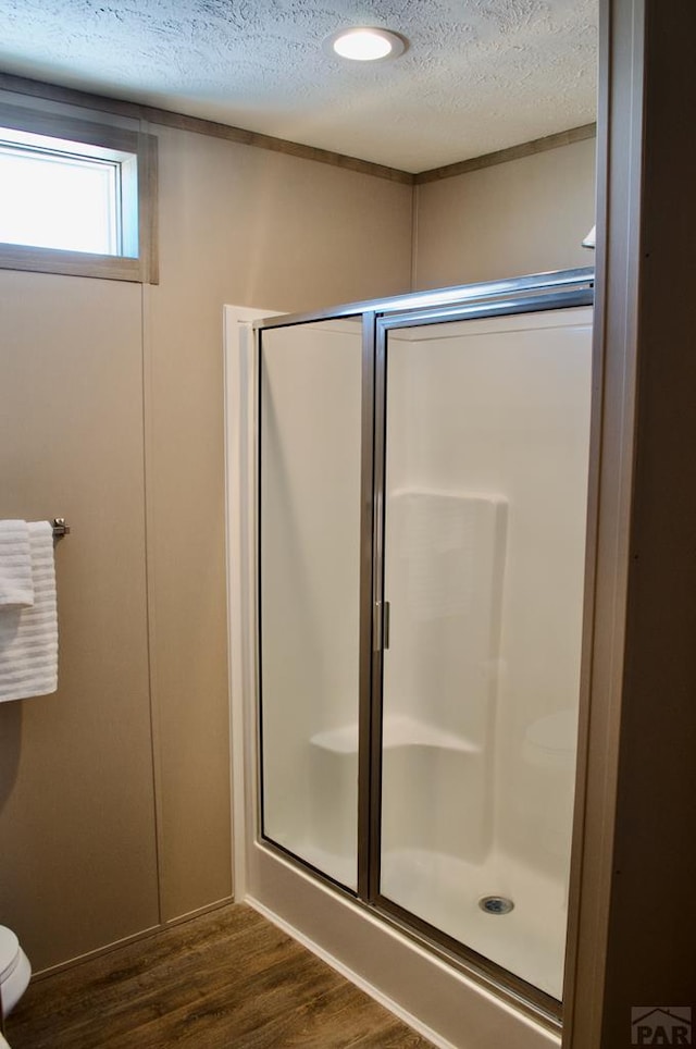 bathroom featuring toilet, a shower stall, a textured ceiling, and wood finished floors