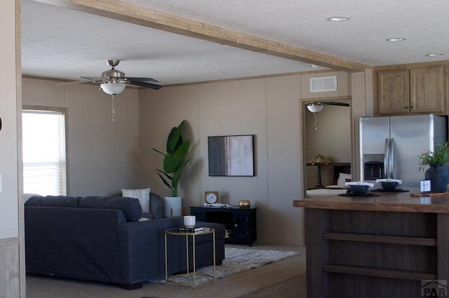 living area with a textured ceiling, beam ceiling, visible vents, and a ceiling fan