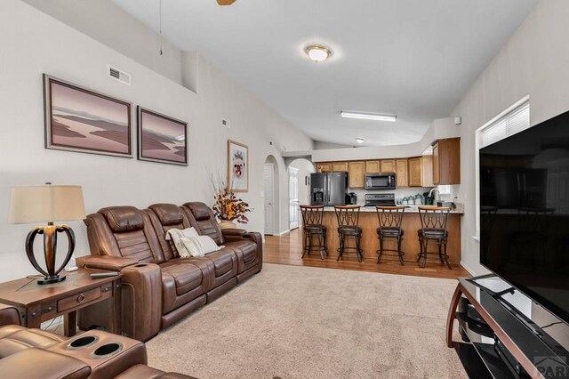 living room with light carpet, visible vents, arched walkways, lofted ceiling, and light wood-type flooring