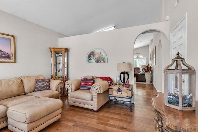 living area with lofted ceiling, arched walkways, and wood finished floors