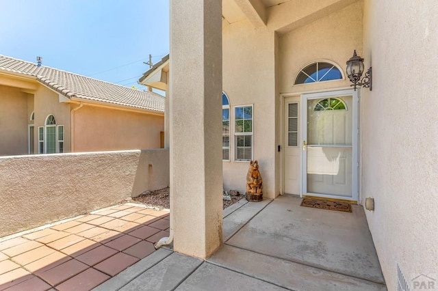 view of exterior entry with a tile roof, a patio, and stucco siding