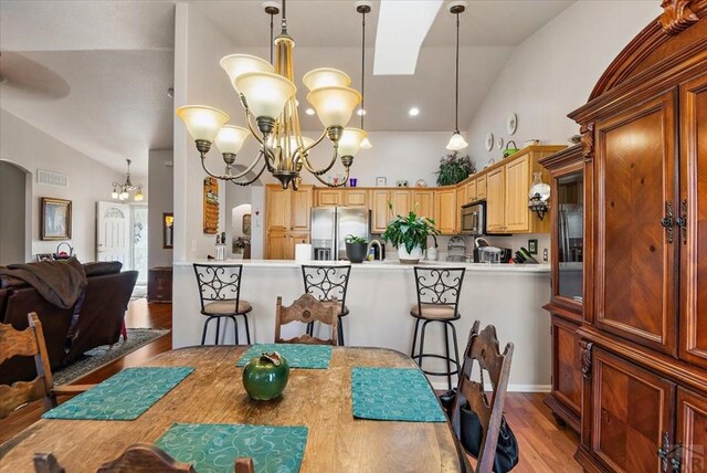 dining room with visible vents, arched walkways, an inviting chandelier, light wood-type flooring, and high vaulted ceiling