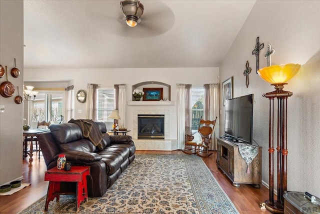 living area featuring ceiling fan, wood finished floors, baseboards, vaulted ceiling, and a tiled fireplace