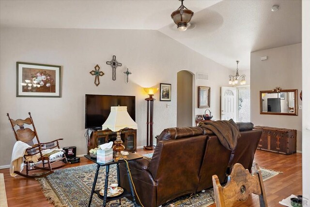 living area with vaulted ceiling, arched walkways, ceiling fan with notable chandelier, and wood finished floors