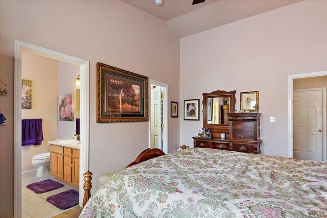 bedroom with lofted ceiling, light tile patterned floors, a sink, and ensuite bathroom