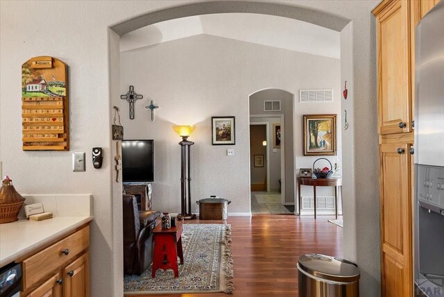 hallway with arched walkways, lofted ceiling, visible vents, and light wood-style floors