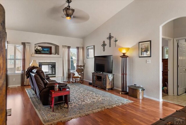 living area with lofted ceiling, a tile fireplace, plenty of natural light, and arched walkways