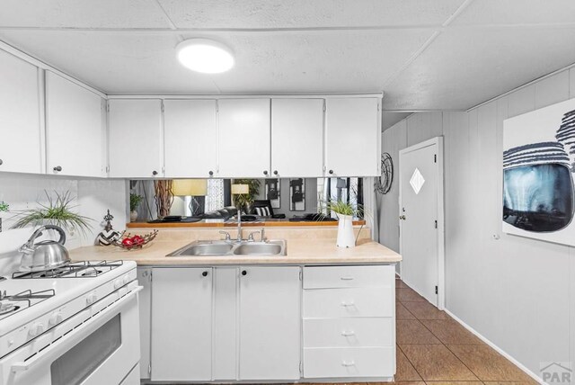 kitchen featuring light countertops, a sink, white gas range oven, and white cabinetry