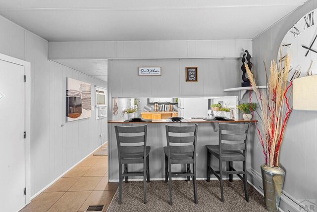 interior space with a peninsula, a kitchen bar, visible vents, and tile patterned floors