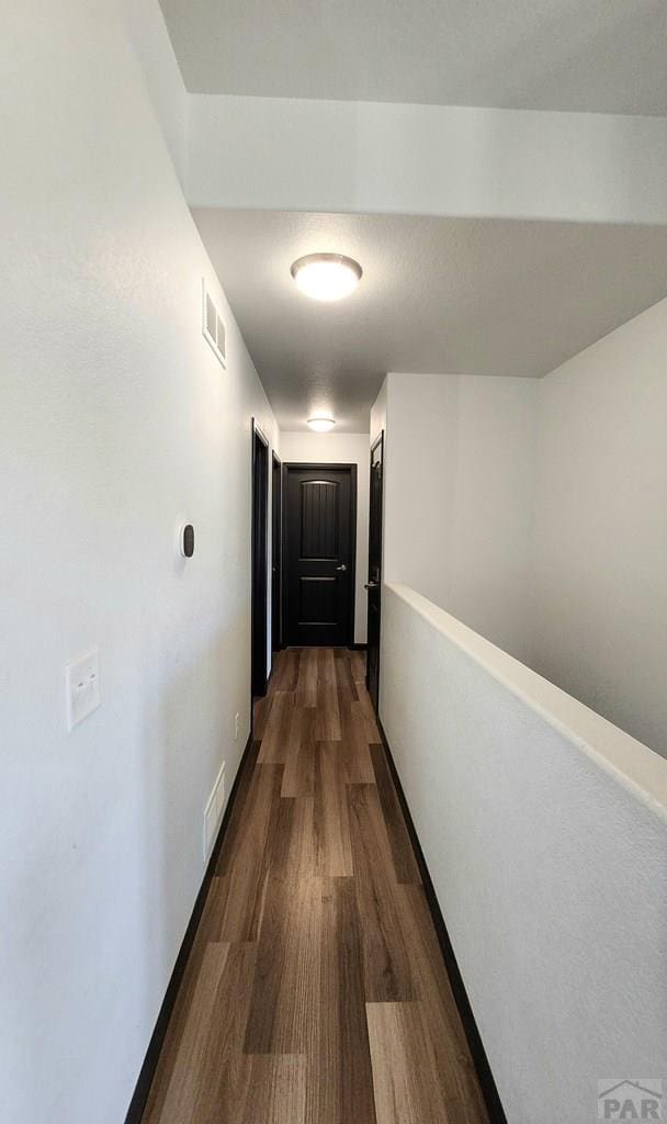 hallway with dark wood-type flooring, visible vents, and baseboards