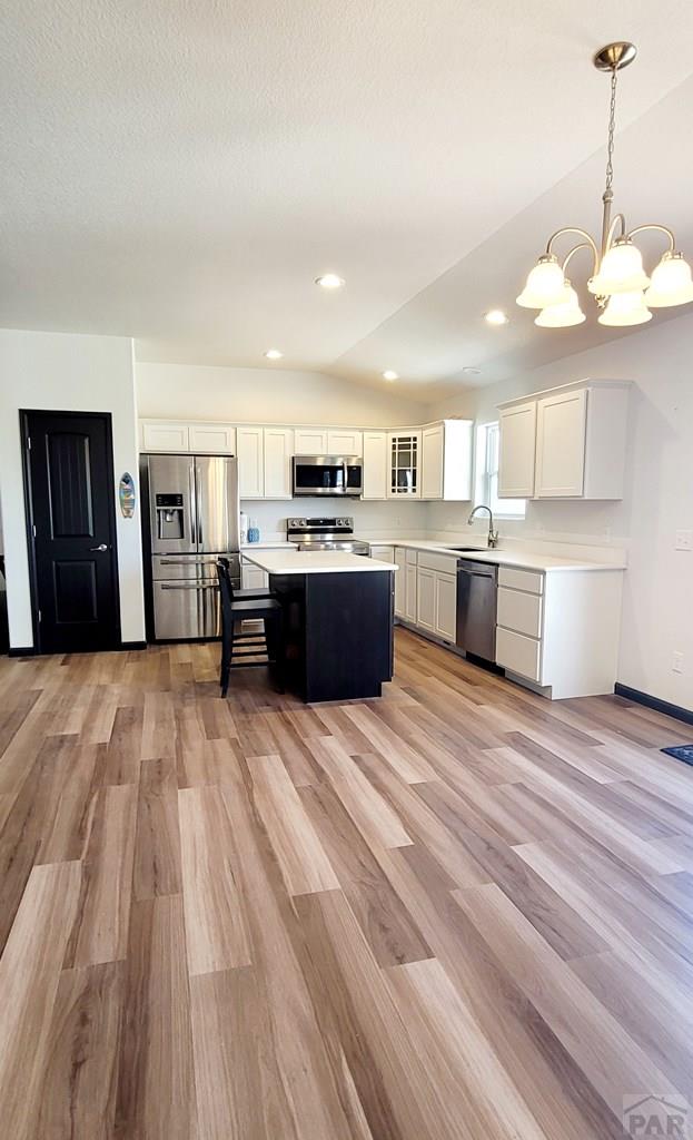 kitchen featuring glass insert cabinets, a center island, decorative light fixtures, stainless steel appliances, and light countertops