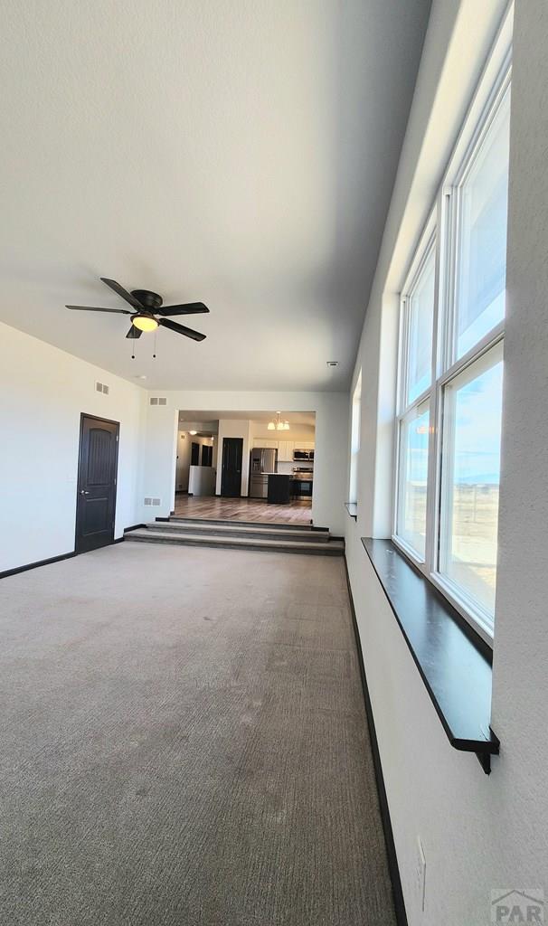 unfurnished living room with ceiling fan, carpet flooring, visible vents, and baseboards