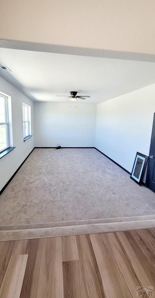 spare room featuring visible vents, baseboards, ceiling fan, wood finished floors, and carpet