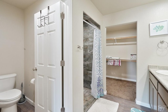 bathroom with toilet, a tile shower, vanity, wood finished floors, and baseboards