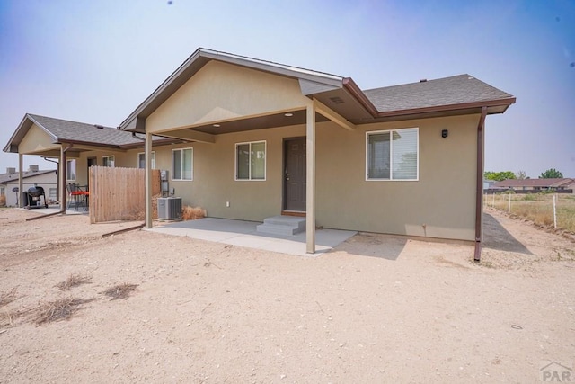 back of property featuring roof with shingles, a patio, stucco siding, central AC unit, and fence