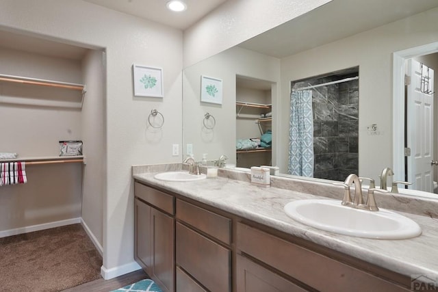 bathroom with a tile shower, double vanity, a sink, and baseboards