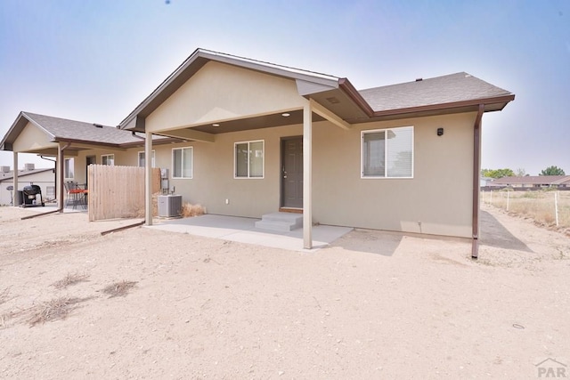 rear view of house with cooling unit, fence, and stucco siding