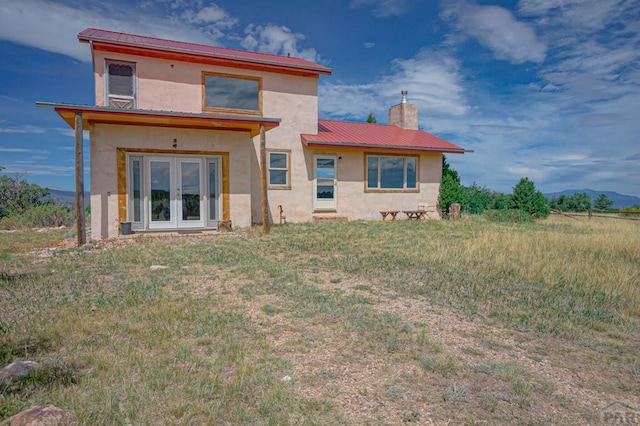 back of property featuring stucco siding, a chimney, metal roof, and french doors