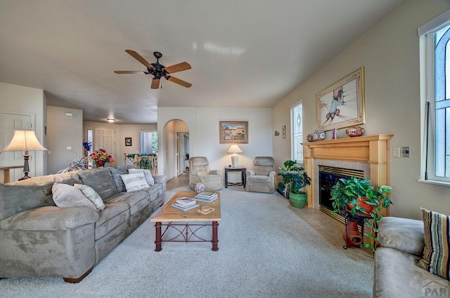 living room featuring light carpet, a fireplace, arched walkways, and a ceiling fan