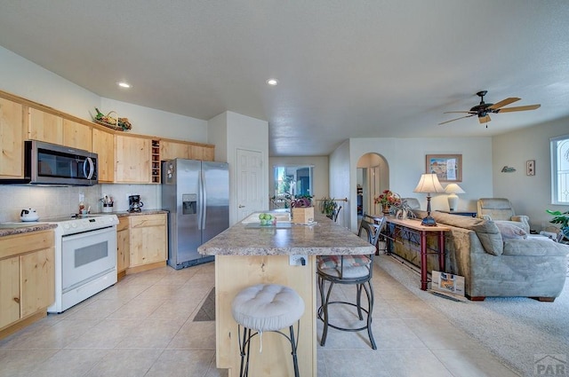 kitchen featuring a kitchen breakfast bar, open floor plan, a kitchen island with sink, stainless steel appliances, and light brown cabinetry