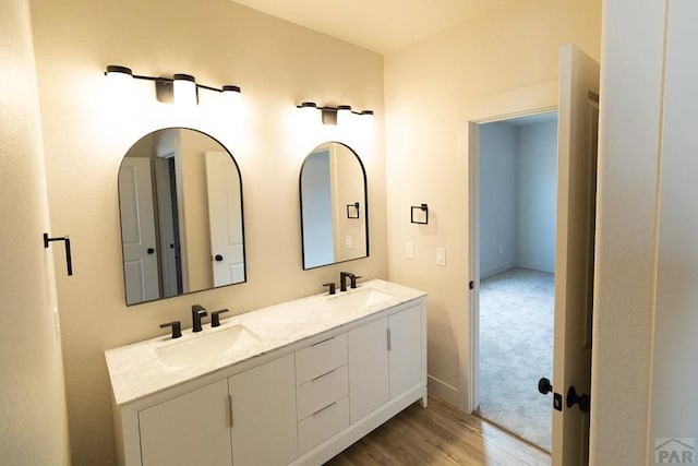 full bathroom with wood finished floors, a sink, baseboards, and double vanity