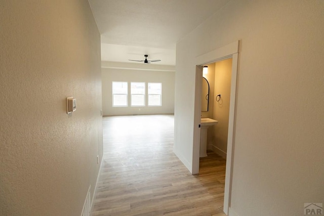 corridor featuring a textured wall, baseboards, and wood finished floors