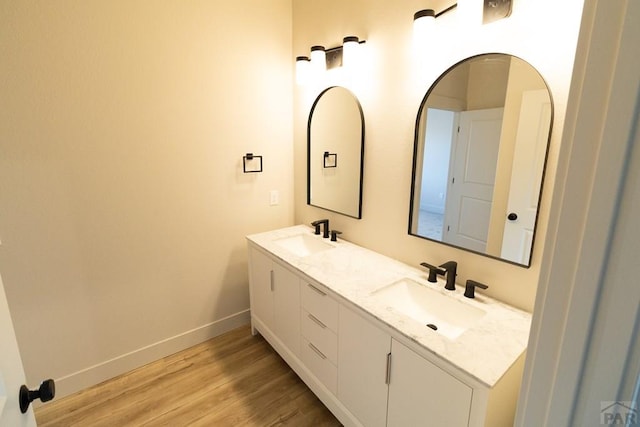 bathroom with double vanity, baseboards, a sink, and wood finished floors