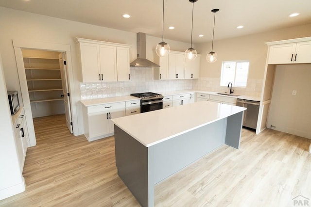 kitchen featuring a sink, light wood-style floors, appliances with stainless steel finishes, a center island, and wall chimney exhaust hood