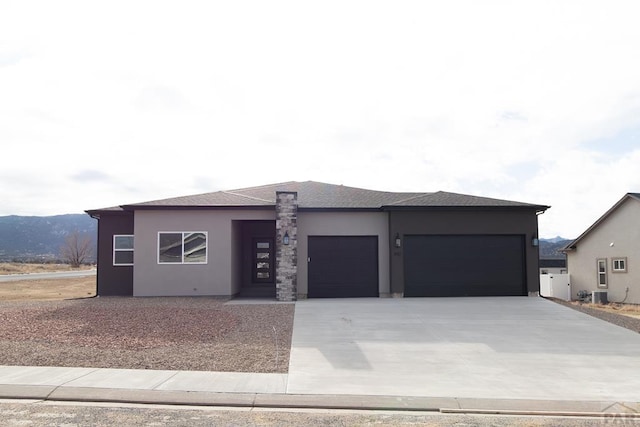 prairie-style home with a garage, driveway, central AC, and stucco siding