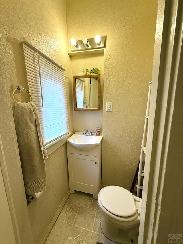 half bath featuring tile patterned flooring, toilet, a textured wall, and vanity