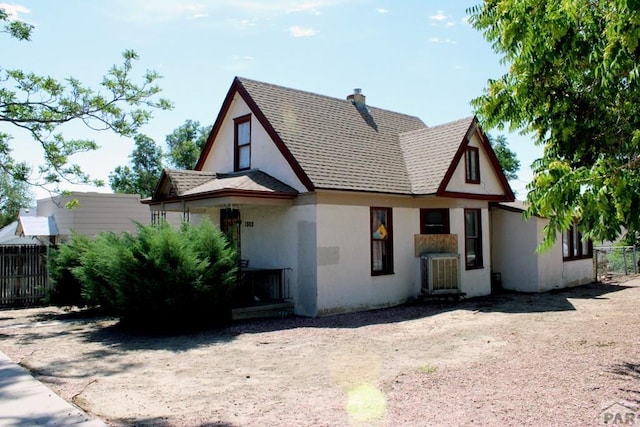 tudor home featuring stucco siding, roof with shingles, and fence