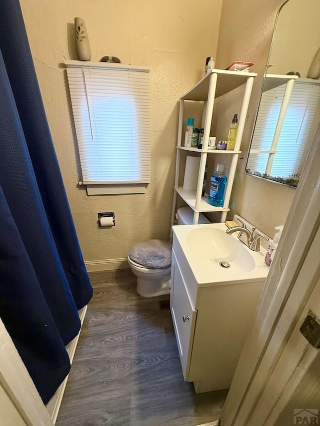 full bathroom with toilet, baseboards, vanity, wood finished floors, and a textured wall