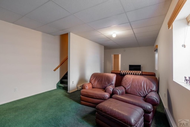 living area with carpet floors, a baseboard radiator, a drop ceiling, and stairway