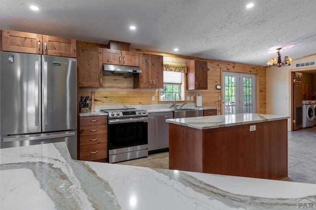 kitchen featuring under cabinet range hood, stainless steel appliances, visible vents, washer and dryer, and brown cabinets