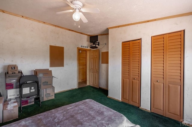 bedroom featuring visible vents, ceiling fan, dark colored carpet, crown molding, and multiple closets