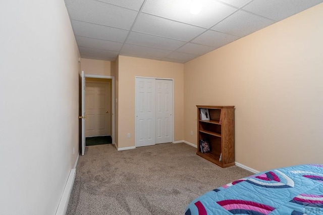 bedroom with light carpet, a closet, baseboards, and a drop ceiling