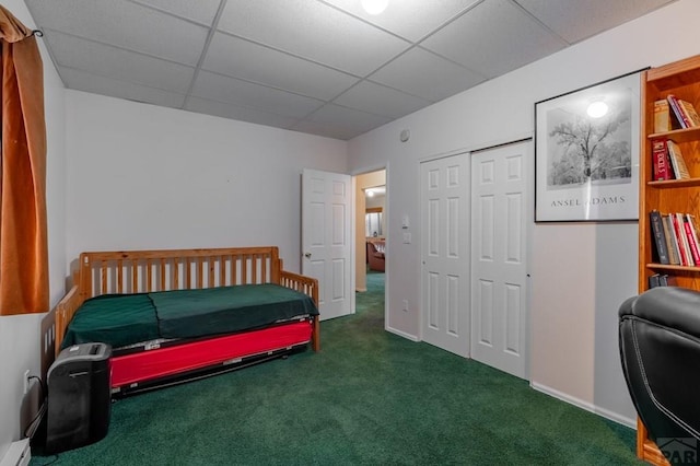 bedroom featuring a closet, dark carpet, a baseboard heating unit, a drop ceiling, and baseboards