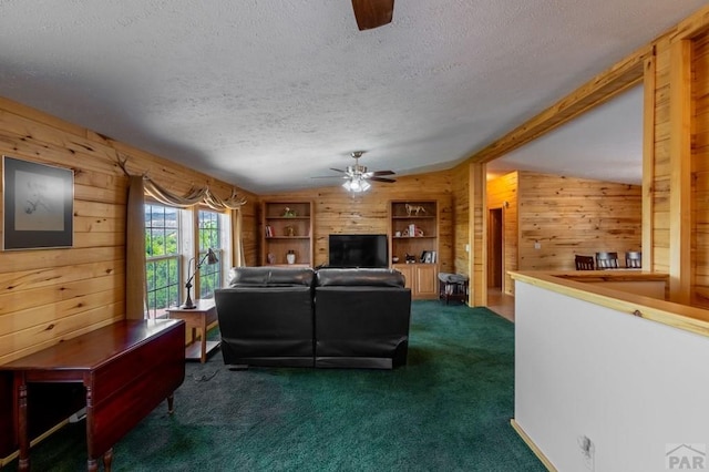 living room featuring a textured ceiling, vaulted ceiling with beams, wood walls, a ceiling fan, and dark colored carpet