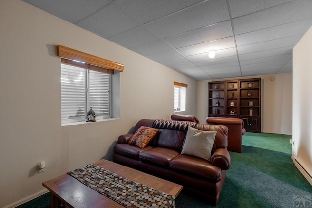 living room featuring dark colored carpet, a drop ceiling, and baseboards