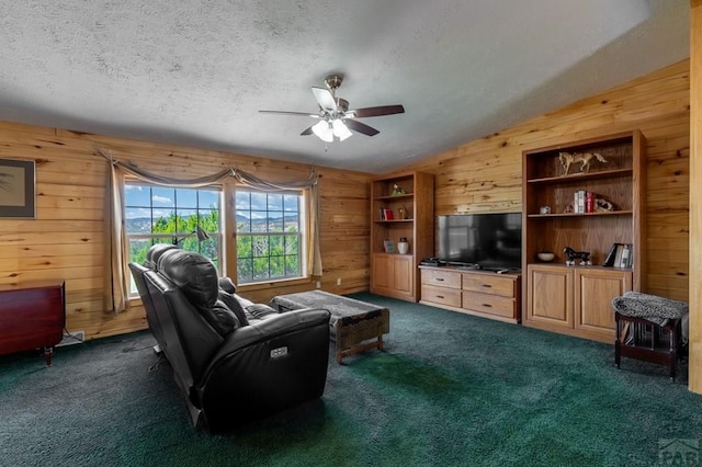 living area featuring dark colored carpet, vaulted ceiling, wood walls, a textured ceiling, and ceiling fan