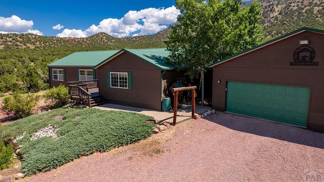 view of front of property featuring an outbuilding, a deck with mountain view, metal roof, a garage, and driveway