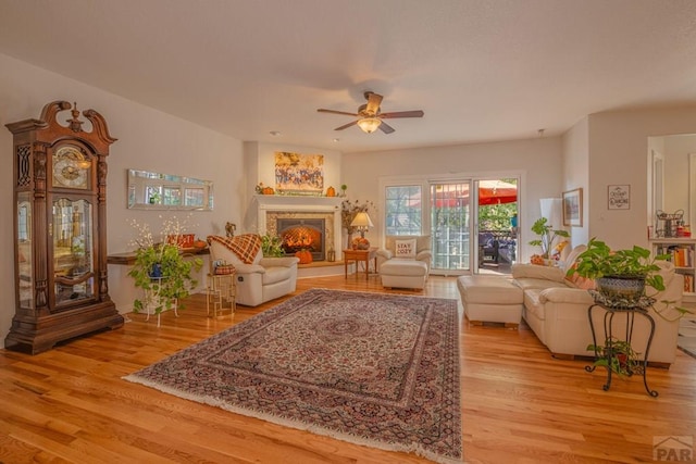 living room with a lit fireplace, light wood finished floors, and a ceiling fan