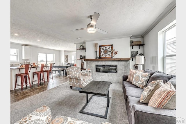 carpeted living room with a tiled fireplace, ceiling fan, crown molding, a textured ceiling, and recessed lighting