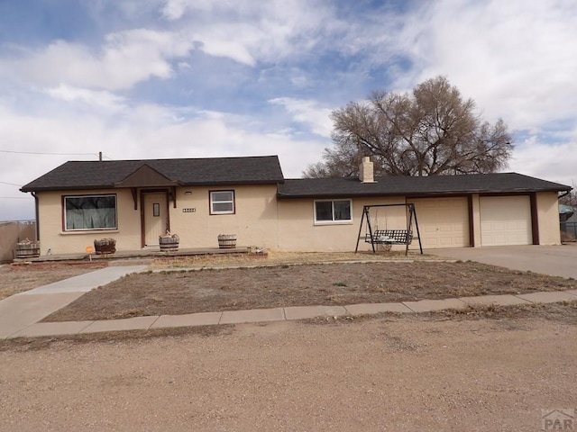 view of front of home featuring concrete driveway, stucco siding, a garage, and a chimney