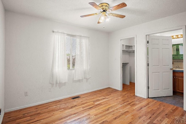 228 S Caddoa Dr, Pueblo West, CO 81007 - unfurnished bedroom with light wood-style flooring, a walk in closet, baseboards, a closet, and a textured ceiling