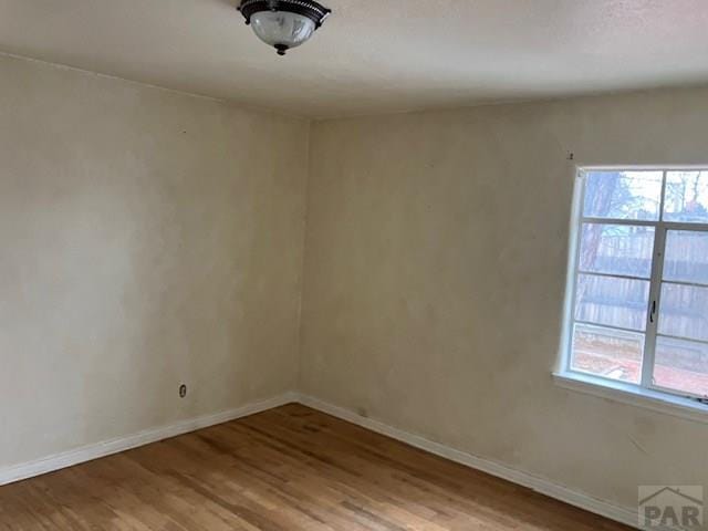 empty room with plenty of natural light, baseboards, and wood finished floors