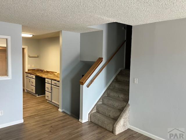 stairway featuring a textured ceiling, wood finished floors, built in study area, and baseboards