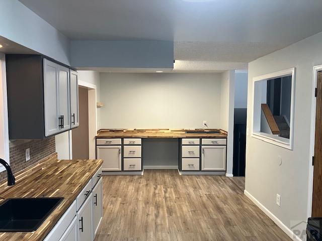 kitchen with gray cabinetry, decorative backsplash, light wood-style floors, a sink, and wood counters